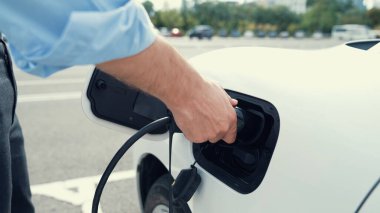 İlerici işadamı, şehir merkezinde dolaşmadan önce şarj cihazından elektrikli arabasına şarj prizi takıyor. Çevre dostu şarj edilebilir araba, sürdürülebilir ve temiz enerjiyle çalışıyor..