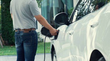 Adamın biri evinde elektrikli araç şarj aletinin fişini çekiyor. İlerici bir yaşam tarzında elektrikli araçların kullanımı, temiz ve sağlıklı bir çevreye katkıda bulunur..