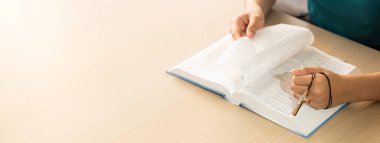 Ahşap masada arka planı bulanık haç tutarken İncil okuyan bir kadının kırpılmış görüntüsü. Umut, din, inanç, Hıristiyanlık ve Tanrı 'nın kutsaması kavramı. Sıcacık. Filizlenen.