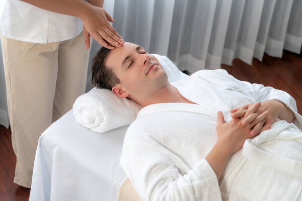 Кавказский мужчина наслаждается расслабляющим анти-стрессовым массажем головы и расслабляющим отдыхом кожи лица в дневном спа современном светлом окружении на роскошном курорте или в спа-салоне отеля. Quiescent