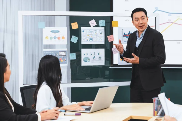 A businessman leader presenting growth Statistics with confident in front of glass whiteboard rounded by female colleagues listening data analyst. Office Conference room meeting. Intellectual.