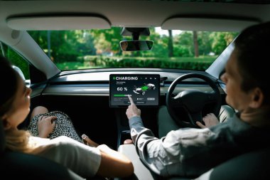 Elektrikli araba sürücüsü, arabadaki uygulama ekranında şarj durumu, menzil ve şarj limitini kontrol ediyor. Akıllı teknoloji aygıtı, EV arabasının araba aküsündeki elektrik depolama verilerini şarj ettiğini gösteriyor..