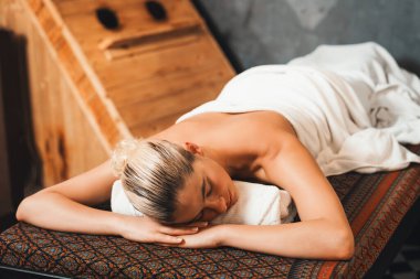 Kafkasyalı güzel bir kadın sauna dolabının önündeki spa yatağında uzanıyor. Genç ve sağlıklı bir kadın sıcak geleneksel spa odasında masaj için bekliyor. Huzur.