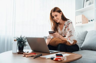 Genç mutlu kadın internetten alışveriş yaparak ürün satın alırken aynı zamanda internet üzerinden online ödeme sistemi ile çevrimiçi mağaza platformundan en yüksek siber güvenlik tarafından korunan ürünler sipariş ediyor.