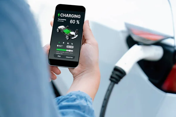 Hand insert EV charger plug into electric vehicle to recharge EV car, battery status display on smartphone EV application. Future alternative clean and sustainable energy for transportation. Perpetual