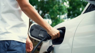 İlerici adam elektrikli aracına elektrik kablosu takıyor. Ev şarj istasyonundan EV arabası. Çevreyi korumak için temiz ve yenilenebilir enerji kullanan elektrikli bir araba. Çevre dostu otomobil.
