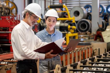 Metal imalatında makine mühendisliği denetleyicisi olarak liderlik örneğini sunan çelik endüstriyel makineyi incelemek için dizüstü bilgisayar kullanan fabrika mühendisi ve asistan..