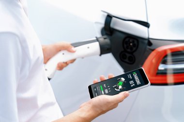 EV 'yi şarj etmek için elektrikli araca EV şarj prizi tak, akıllı telefon EV uygulamasında pil durumu görüntüsü. Ulaşım için alternatif temiz ve sürdürülebilir enerji. Kalıcı