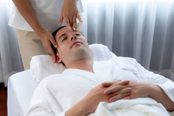 Caucasian man enjoying relaxing anti-stress head massage and pampering facial beauty skin recreation leisure in dayspa modern light ambient at luxury resort or hotel spa salon. Quiescent