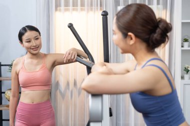 Enerjik ve güçlü atletik Asyalı kadın evde spor arkadaşı ya da antrenörü ile birlikte eliptik koşu makinesiyle koşuyor. Formda fiziğin takibi ve sağlıklı yaşam tarzına bağlılık. Kuvvetli