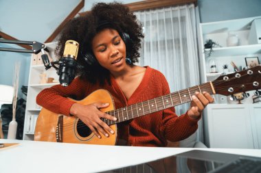 Genç Afrikalı Amerikalı müzisyenin sunucu kanalı gitar çalıyor, şarkı söylüyor, stüdyoda dizüstü bilgisayardan yayın yapıyor. Kulaklık dekorasyonu ve mikrofon kaydı. Tatlandırıcı.