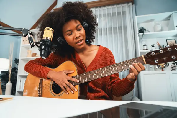 Genç Afrikalı Amerikalı müzisyenin sunucu kanalı gitar çalıyor, şarkı söylüyor, stüdyoda dizüstü bilgisayardan yayın yapıyor. Kulaklık dekorasyonu ve mikrofon kaydı. Tatlandırıcı.