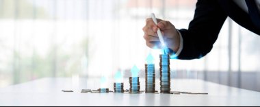 Dijital grafik göstergeli bozuk para yığını iş yatırımını ve ekonomik büyümeyi sembolize ediyor. Finansal hedefe ulaşmak ve kâr sağlamak için finansal planlama yapan bir iş adamı. Kurnaz.