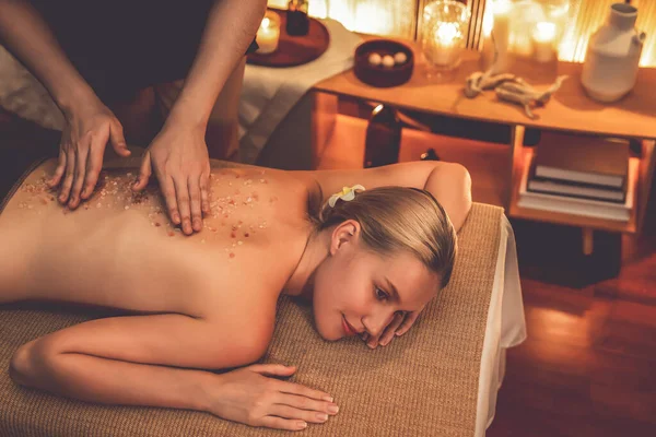Woman customer having exfoliation treatment in luxury spa salon with warmth candle light ambient. Salt scrub beauty treatment in Health spa body scrub. Quiescent