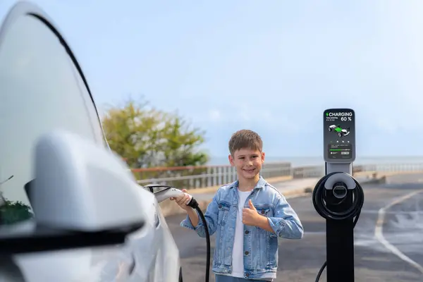 Ev充電ステーションから環境に優しい電気自動車を充電する小さな少年 Evカーロード旅行は クリーンな再生可能で持続可能なエネルギーによって動力を与えられた代替車によって海岸を移動します パーペチュアル — ストック写真