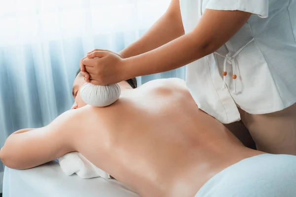 Hot herbal ball spa massage body treatment, masseur gently compresses herb bag on man body. Tranquil and serenity of aromatherapy recreation in day lighting ambient at spa salon. Quiescent