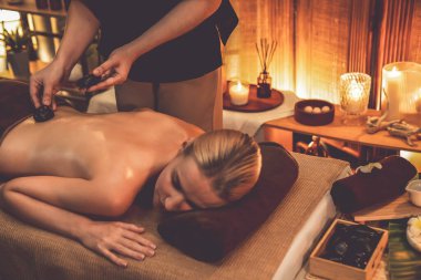 Lüks tatil köyündeki kaplıcalarda sıcak taş masajı, sıcak mum ışığı, spa bazalt taşı masajının keyfini çıkaran mutlu kadın müşteriler, rahatlatıcı bir sıcaklıkla vücudun üzerinde süzülüyorlar. Sessiz.