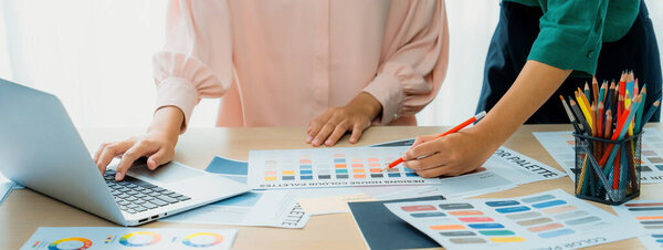 Обрезанное изображение двух молодых женщин красивый графический дизайнер выбрать цвет от цвета неба с помощью ноутбука на столе с рабочими инструментами и оборудованием разбросаны вокруг в современном офисе. Варфоломей.