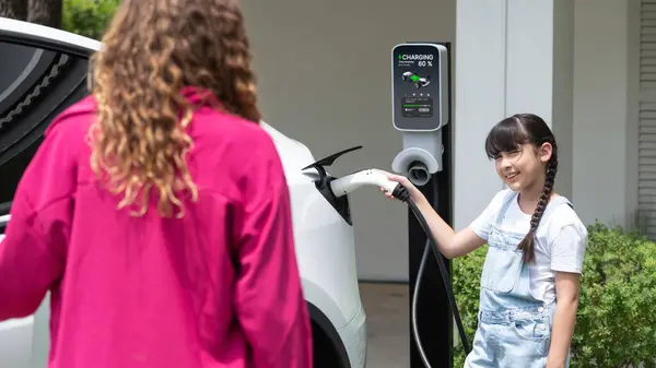 幸せな小さな少女は 母親がEv充電ステーションから電気自動車を充電するのを助けるため 環境にやさしいエネルギーの持続可能性について学びます Ev車とモダンファミリー パノラマシンクロノス — ストック写真