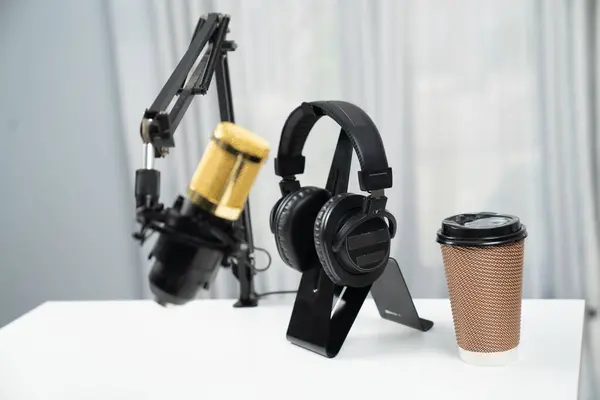 All stuff sets of live streaming standing on white desk consist of microphone, headsets, coffee cup, smartphone, glasses and notebook. Concept of equipment for coaching host channel. Tastemaker.