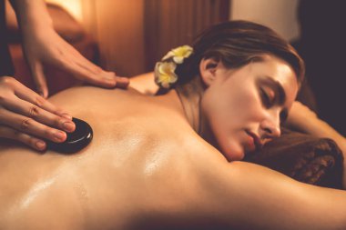 Lüks tatil köyündeki kaplıcalarda sıcak taş masajı, sıcak mum ışığı, spa bazalt taşı masajının keyfini çıkaran mutlu kadın müşteriler, rahatlatıcı bir sıcaklıkla vücudun üzerinde süzülüyorlar. Sessiz.