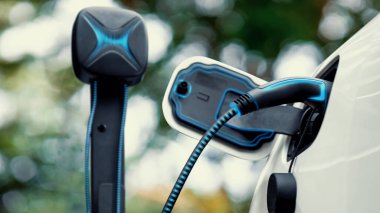 Elektrikli araba, çevre yeşil parkındaki elektrik kablosu ve yeşillik yeşili yeşillik yapraklarıyla şarj etmek için şarj istasyonuna bağlandı. Geleceğin yenilikçi her arabası ve enerji sürdürülebilirliği.