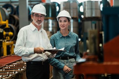 Metal imalatında makine mühendisliği denetleyicisi olarak liderlik örneğini sunan çelik endüstriyel makineyi incelemek için dizüstü bilgisayar kullanan fabrika mühendisi ve asistan..