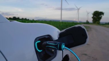 Elektrikli araba, EV şarj istasyonundan enerji alıyor. Rüzgar türbini çiftliğinde EV şarj kablosu kablosunun fütüristik akıllı batarya durum hologramını gösteriyor. Alternatif temiz enerji sürdürülebilirliği. İnceleyin