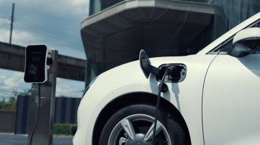 İlerici iş kadını şehir merkezinde dolaşmadan önce şarj cihazından elektrikli arabasına şarj prizi takıyor. Çevre dostu şarj edilebilir araba, sürdürülebilir ve temiz enerjiyle çalışıyor..