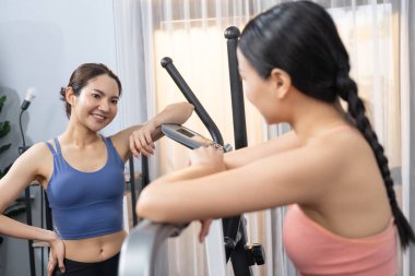 Enerjik ve güçlü atletik Asyalı kadın evde spor arkadaşı ya da antrenörü ile birlikte eliptik koşu makinesiyle koşuyor. Formda fiziğin takibi ve sağlıklı yaşam tarzına bağlılık. Kuvvetli