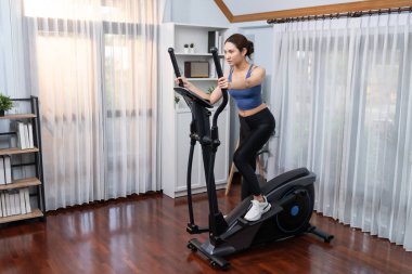 Enerjik ve güçlü atletik Asyalı kadın evde eliptik koşu makinesiyle koşuyor. Formda fiziğin takibi ve ev çalışması ve eğitimle sağlıklı yaşam tarzına bağlılık. Kuvvetli