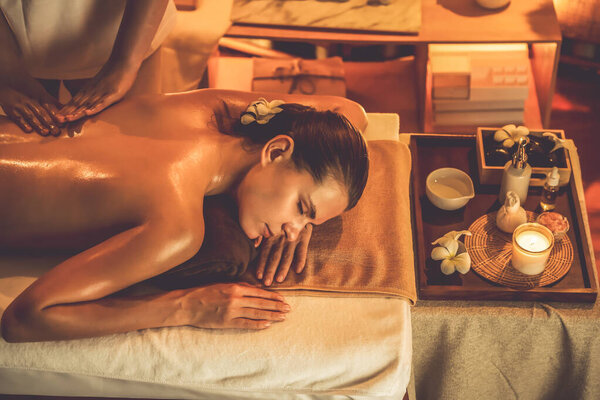 Caucasian woman customer enjoying relaxing anti-stress spa massage and pampering with beauty skin recreation leisure in warm candle lighting ambient salon spa at luxury resort or hotel. Quiescent