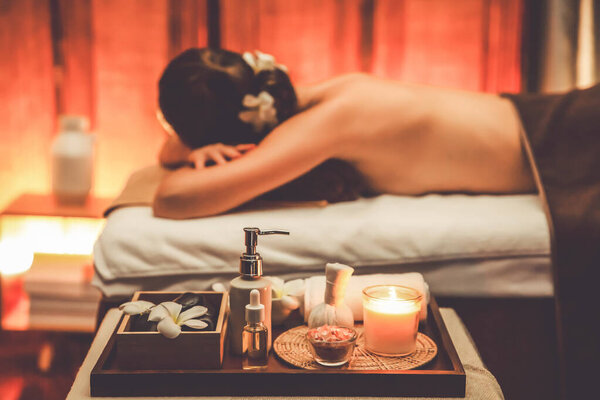 Aromatherapy massage ambiance or spa salon composition setup with focus decor candles and spa accessories on blurred woman enjoying blissful aroma spa massage in resort or hotel background. Quiescent