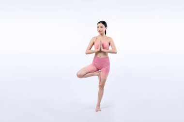 Spor kıyafetli Asyalı bir kadın antrenman yaparken ayakta durarak yoga egzersizi yapıyor. Sağlıklı vücut bakımı ve meditasyon yoga yaşam tarzı izole bir arka planda. Kuvvetli