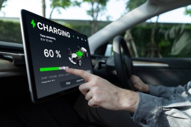 Elektrikli araba sürücüsü, arabadaki uygulama ekranında şarj durumu, menzil ve şarj limitini kontrol ediyor. Akıllı teknoloji aygıtı, EV arabasının araba aküsündeki elektrik depolama verilerini şarj ettiğini gösteriyor..