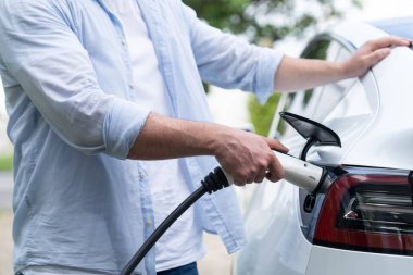 Çevre dostu bilinçli adam EV şarj istasyonundan modern elektrikli aracı şarj ediyor. EV araba teknolojisi gelecekteki sürdürülebilirlik için alternatif ulaşım aracı olarak kullanılıyor. Eşzamanlama