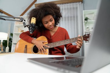 Genç Afrikalı Amerikalı müzisyenin sunucu kanalı gitar çalıyor, şarkı söylüyor, stüdyoda dizüstü bilgisayardan yayın yapıyor. Kulaklık dekorasyonu ve mikrofon kaydı. Tatlandırıcı.