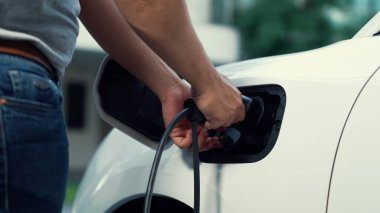 İlerici adam evindeki elektrikli aracın aküsüne emisyonsuz güç bağlantısı kuruyor. Elektrikli araç elektrik istasyonundan EV araba aküsüne kabloyla şarj oluyor.
