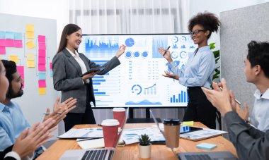 İş adamları TV ekranında başarılı bir sunum veya veri analizi toplantısından sonra kutlama yapıyorlar. Mutlu takım ofis odasında toplanıyor, kutlama jestleriyle işbirliği için tezahürat yapıyorlar. Uyum