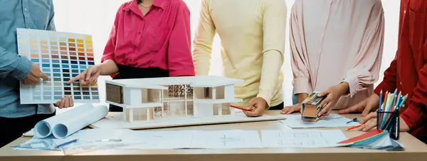建築家がブループリントと家のモデルを置いたテーブルに青写真の文書を書いている間 プロの建築家チームが家の色の選択についてのブレインストーミングのイメージ ヴァリーゲート — ストック写真