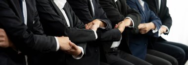 Panoramik afiş ekibi sırada oturup el ele vererek başarılı iş ortaklığını ve iş bulma için profesyonel sinerjiyi, İK işe alım konseptini sembolize ediyor. Kurnaz.