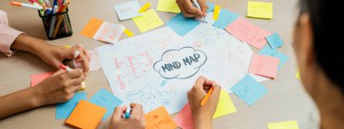 Profesyonel başlangıç grubu zihin haritası kullanarak yaratıcı pazarlama fikrini paylaşıyor. Genç yetenekli iş adamları yapışkan notlar yazarken beyin fırtınası planı yapıyorlar. Eline odaklan. - Yakın çekim. Değiştirilmiş.