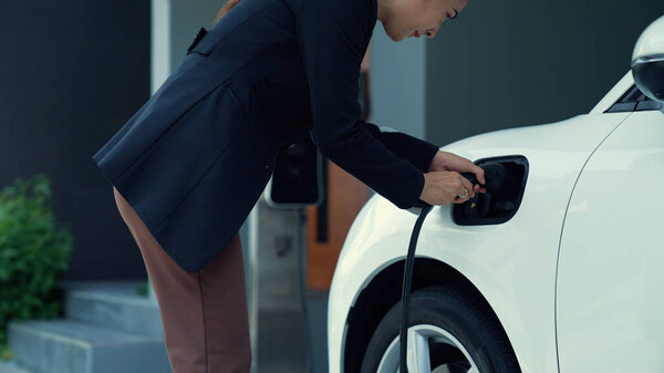 A woman unplugs the electric vehicles charger at his residence. Concept of the use of electric vehicles in a progressive lifestyle contributes to a clean and healthy environment.