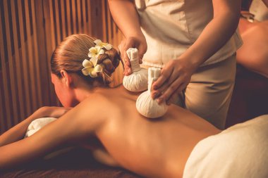 Sıcak bitkisel top spa masaj vücut tedavisi, masör kadın vücuduna nazikçe şifalı bitki torbası bastırıyor. Aromaterapi tesisinin sakinliği ve dinginliği kaplıca salonundaki mumların sıcacık ışığında. Sessiz.