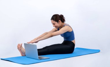 İnternetteki videodan alınan talimatlara göre spor kıyafeti giymiş genç Asyalı bir kadın spor egzersizinden önce geriniyor. Sağlıklı atletik bir kadınla vücut egzersizi izole bir zeminde ısınıyor. Kuvvetli