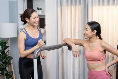 Enerjik ve güçlü atletik Asyalı kadın evde spor arkadaşı ya da antrenörü ile birlikte eliptik koşu makinesiyle koşuyor. Formda fiziğin takibi ve sağlıklı yaşam tarzına bağlılık. Kuvvetli