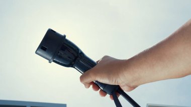 Yakın plan, çevresel kaygılar için alternatif sürdürülebilir temiz ve yeşil enerji kavramı olarak arka planda gün ortası gökyüzü ile elektrikli araç için bir EV kapsülü kavrıyor.