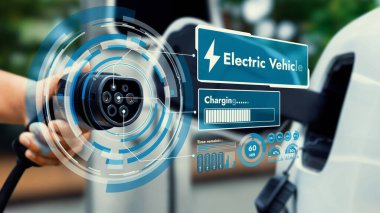Kameranın önündeki EV şarj aletine odaklan. Bulanık arka planda akıllı batarya durum hologramını göster. Karbondioksit salınımını azaltmak için temiz enerji kullanan elektrikli araba şarjı.