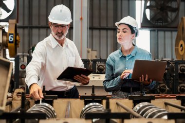 Metal imalatında makine mühendisliği denetleyicisi olarak liderlik örneğini sunan çelik endüstriyel makineyi incelemek için dizüstü bilgisayar kullanan fabrika mühendisi ve asistan..