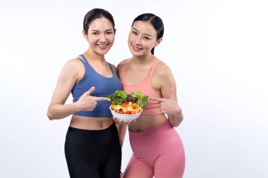 Spor kıyafetli iki genç Asyalı kadın ellerinde meyve ve sebze dolu salata kasesi tutuyorlar. Doğal gençlik ve formda yaşam tarzı izole edilmiş arka planda dengeli beslenen insanlar. Kuvvetli